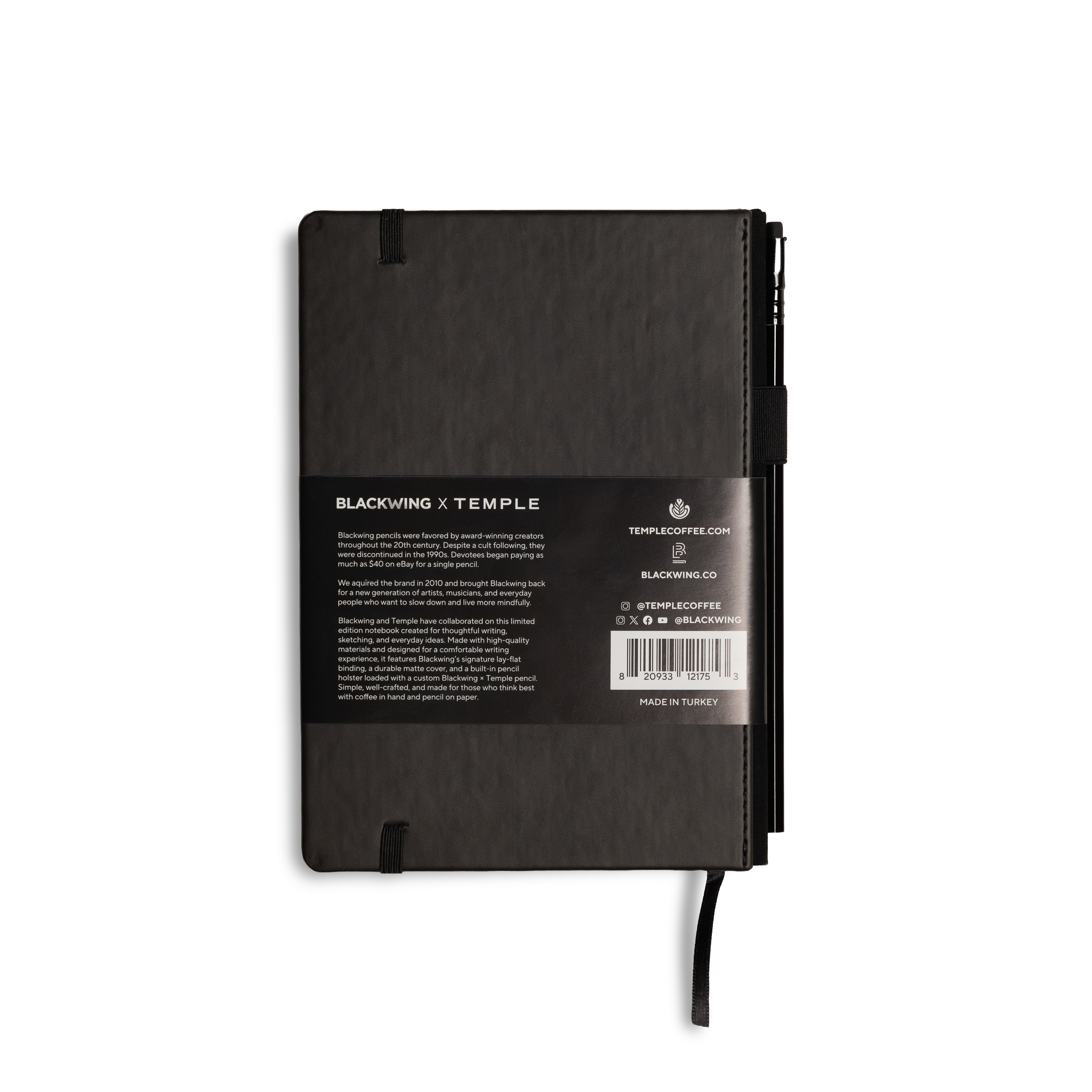 A black hardcover notebook with a black label on the back, featuring a black elastic closure and a black ribbon bookmark, photographed on a solid white background.