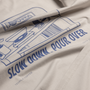 Close-up of a light beige or off-white fabric surface with a blue line-art graphic and the text 'SLOW DOWN POUR OVER' plus 'TEMPLE COFFEE' printed on it.